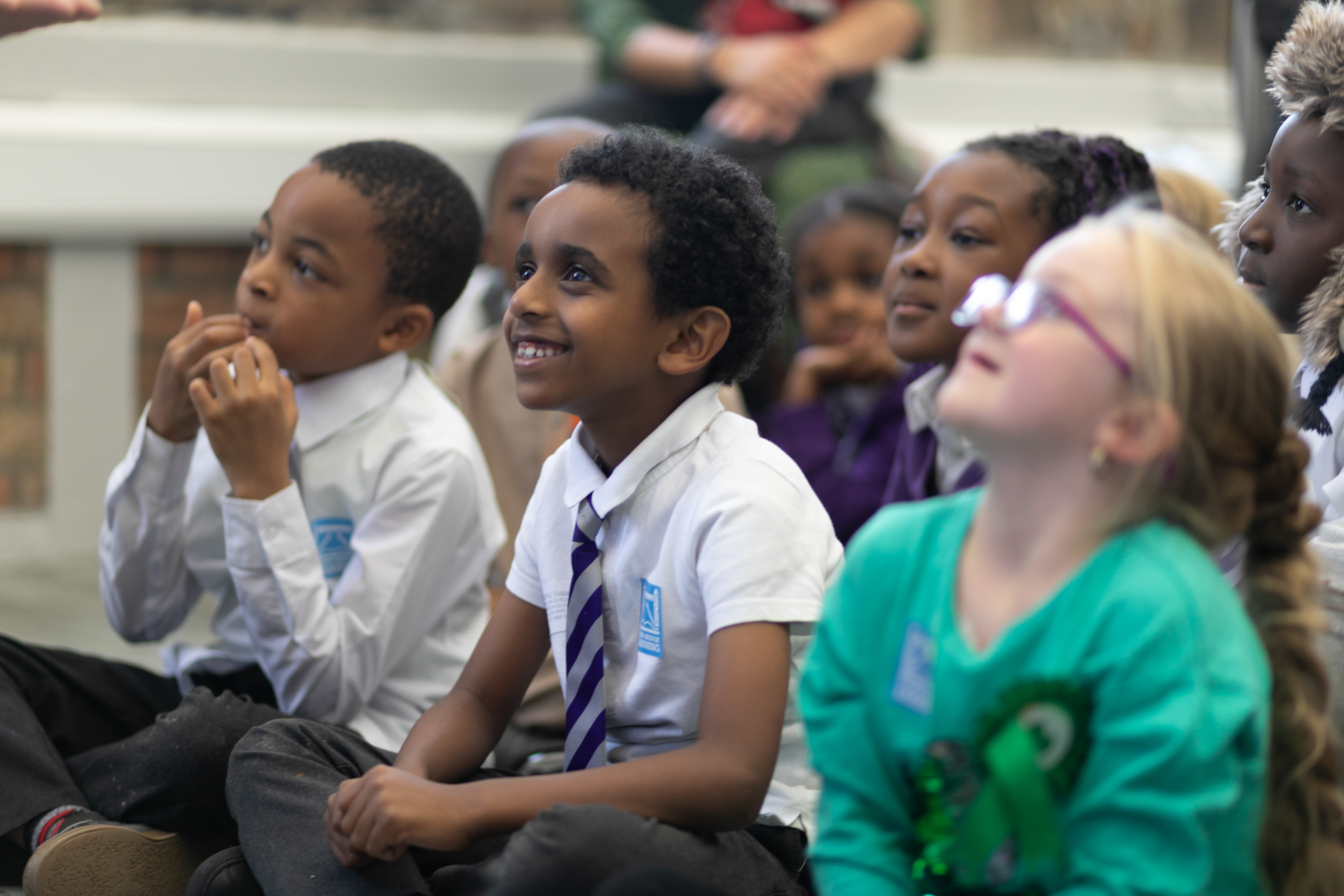 School students sit on the floor looking up and smiling