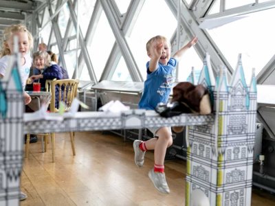 Boy throws paper aeroplane towards model Tower Bridge, inside the Walkways
