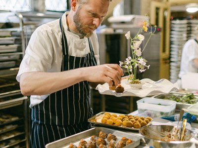 A chef in a blue striped apron is busy plating up some delicious looking canapes. 