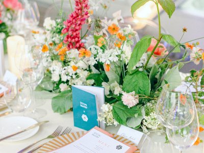 A table laid beautifully for dinner with white, green and pink flowers, place settings and menus. 