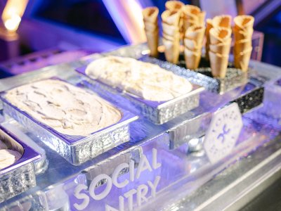 An ice cream station at an event. There are three big containers of ice cream and some cones. 