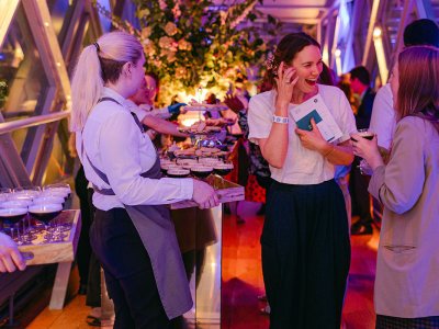 An evening event in the Walkways. Two guests are talking and laughing and a server is holding drinks.