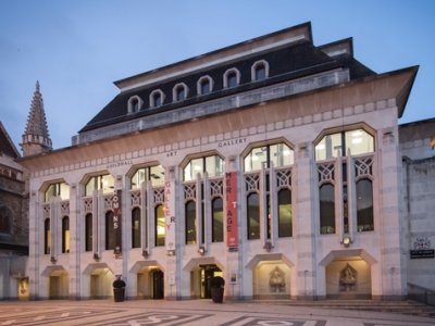 Guildhall Art Gallery at dusk, it is a white stone building with arching windows and long pillars and a dark roof.