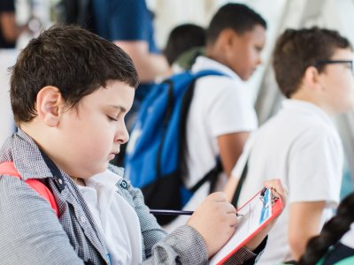 A boy draws on a piece of paper during a learning activity inside the Tower Bridge Walkways