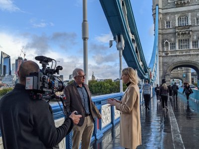 An interview between a man and a woman is filmed on the pavement of Tower Bridge
