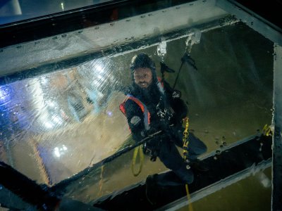 A view through the Glass Floor of a man  in a harness cleaning the underside