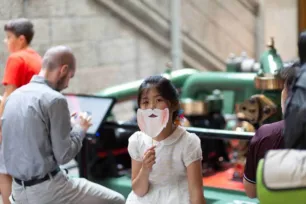 A child in a dress holds a paper beard like Horace Jones' to her face.