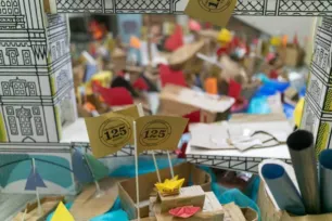 Small cardboard and origami boats crowd a model Tower Bridge