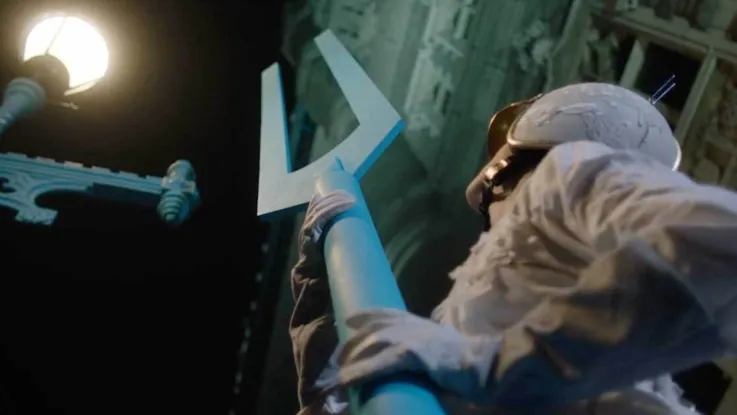 Workers in protective suits hold a large blue forked pole under a lamppost.