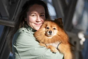 A woman smiles as she holds a fluffy pomeranian up to her chin