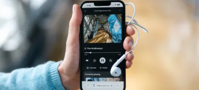 A person holding a phone with the Tower Bridge Audio Tour on it, headphones are plugged into the phone
