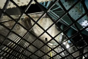 A dark large tavernous space with curved brick stairs seen through a grid of grating.