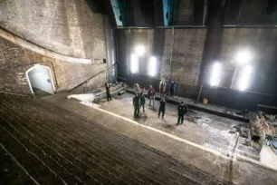 A dark large cavernous space with curved brick stairs, looking down at people from above.