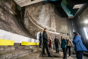 A dark large cavernous space with curved brick stairs. People are at the bottom of the stairs looking up.