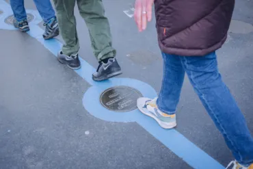 People walking along the Blue line at Tower Bridge with bronze plaques set on surface.