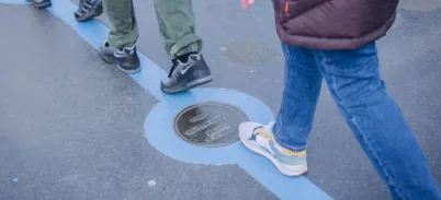 People walking along the Blue line at Tower Bridge with bronze plaques set on surface.