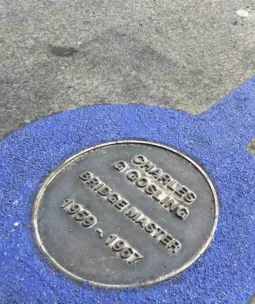 A plaque on the pavement of Tower Bridge with a blue ring painted round ti - Charles G Gosling, Bridge Master 1959 - 1967 is written on the plaque.