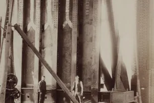 A sephia image of two Victorian workers stading in front of a vast metal structure.