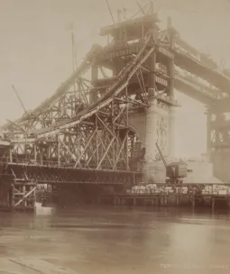 A sephia photo of Tower Bridge being built with it's steel, grid-like structure exposed.