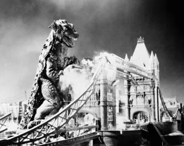 A black and white still of Gorgo - a large dinosaur-like monster towers over Tower Bridge.