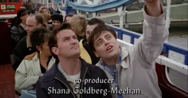 Joey and chandler sitting on an open-air tour bus crossing Tower Bridge taking a selfie.