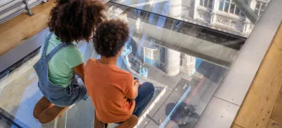 Two kids kneeling on the Glass Floors and  looking down to the road.