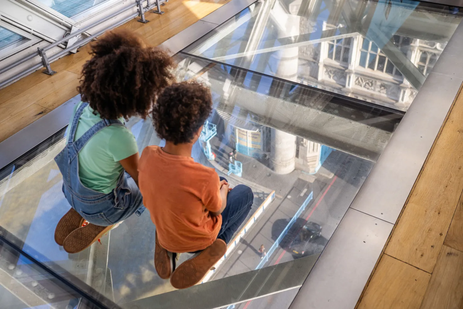 Two kids kneeling on the Glass Floors and  looking down to the road.