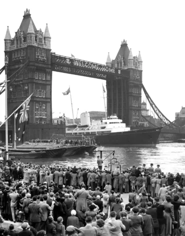 Old black and white photo of a yacht sailing through Tower Bridge