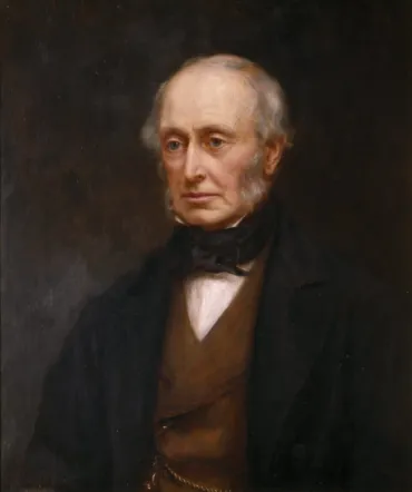 A portrait of an elderly man wearing a Victorian suit and waistcoat. He has sideburns and a bald head.