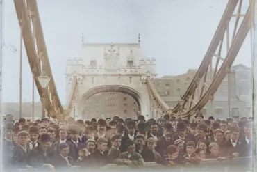 Historic photograph of a large crowd gathered on Tower Bridge during its public opening day in 1894, with the iconic Gothic-style towers and suspension chains prominently visible in the background.