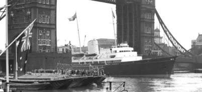 Old black and white photo of a yacht sailing through Tower Bridge