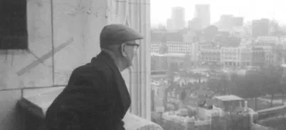 A black and white photo of man at the top of Tower Bridge looking out at the view of London