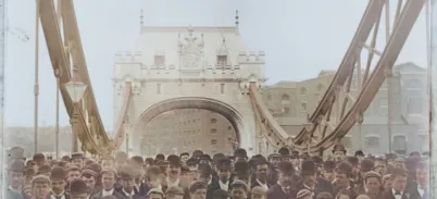 Historic photograph of a large crowd gathered on Tower Bridge during its public opening day in 1894, with the iconic Gothic-style towers and suspension chains prominently visible in the background.