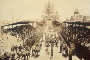 Historic photograph of Tower Bridge opening ceremony in London, showing horse-drawn carriages, large crowds in grandstands, and the bridge towers in the background.