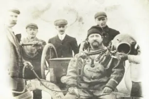 A black and white photo of 5 men, one of them dressed in a diver suit