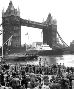 Old black and white photo of a yacht sailing through Tower Bridge