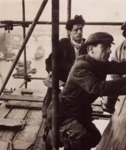 Historic photo of three workers on the roof of Tower Bridge engaged in construction atop scaffolding.