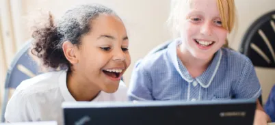 Two school children looking at a computer, smiling