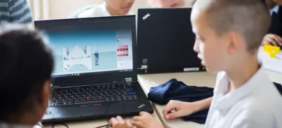 Two children use a laptop showing a simple design of a bridge