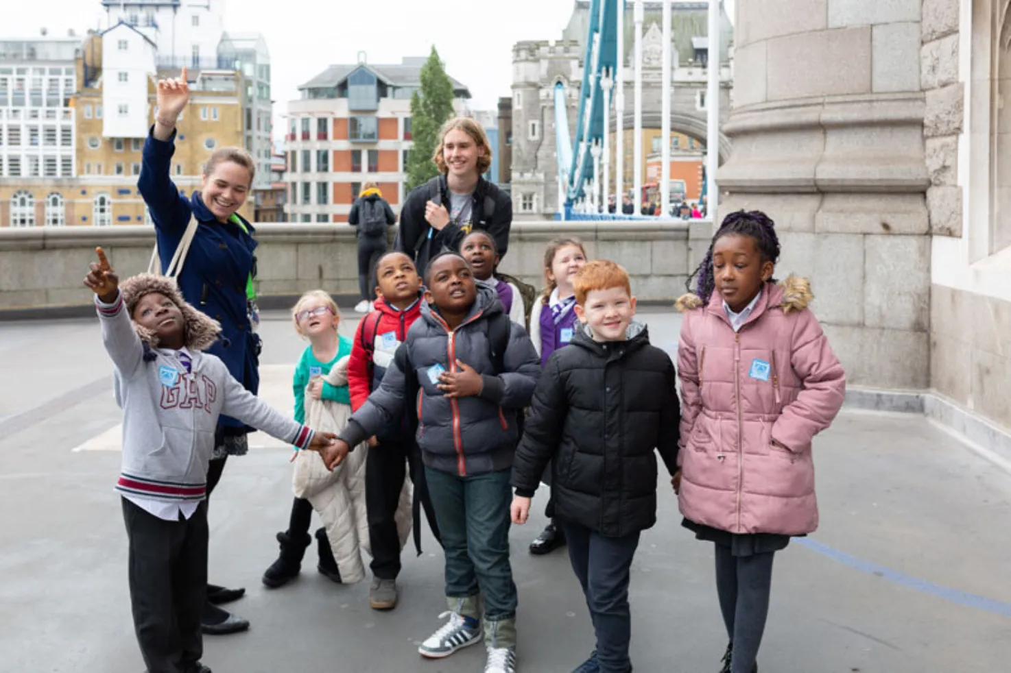 A group of schoolchildren and adults smile and wave, as they stand on Tower Bridge.