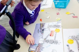 A child in a purple school jumper moves pictures on a table showing a bus jumping over a gap in Tower Bridge.