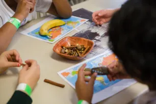A table with chocolate biscuits, a banana and maps, with children's hands holding biscuits