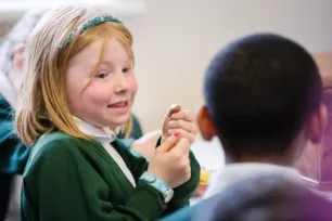 A girl in a green jumper smiles at another school child