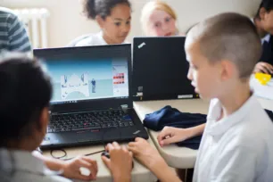 Two children use a laptop showing a simple design of a bridge