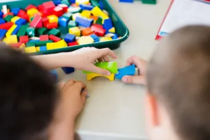 A tray of colourful building blocks, two children's hands are holding some together to make a bridge.