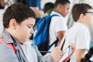 A teenage schoolchild writes on a clipboard while other children look out of the Tower Bridge walkway window