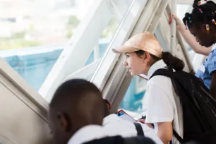 Three schoolchildren look out of the window of a Tower Bridge walkway