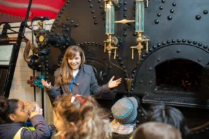 A woman giving a guided tour to a group of school kids at the Engine Rooms of Tower Bridge.