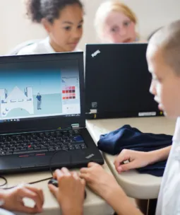 Two children use a laptop showing a simple design of a bridge