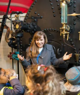 A woman giving a guided tour to a group of school kids at the Engine Rooms of Tower Bridge.